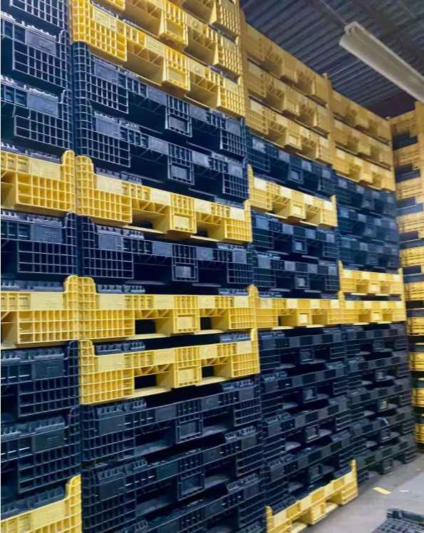 Stacks of collapsed black and yellow plastic bulk containers in a warehouse.
