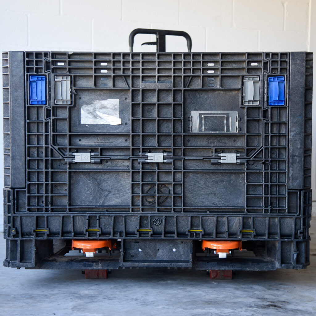 Used black collapsible bulk container upright with its front access door closed and a pallet jack underneath.