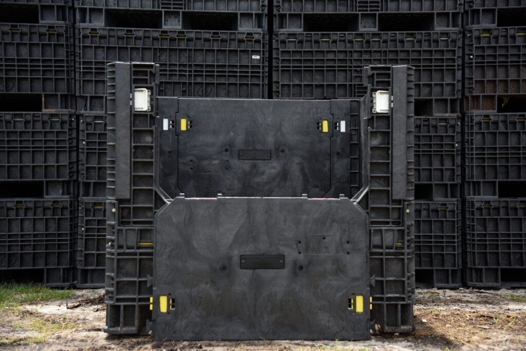 Used black collapsible bulk container with its front access door lowered, pictured before stacked containers.